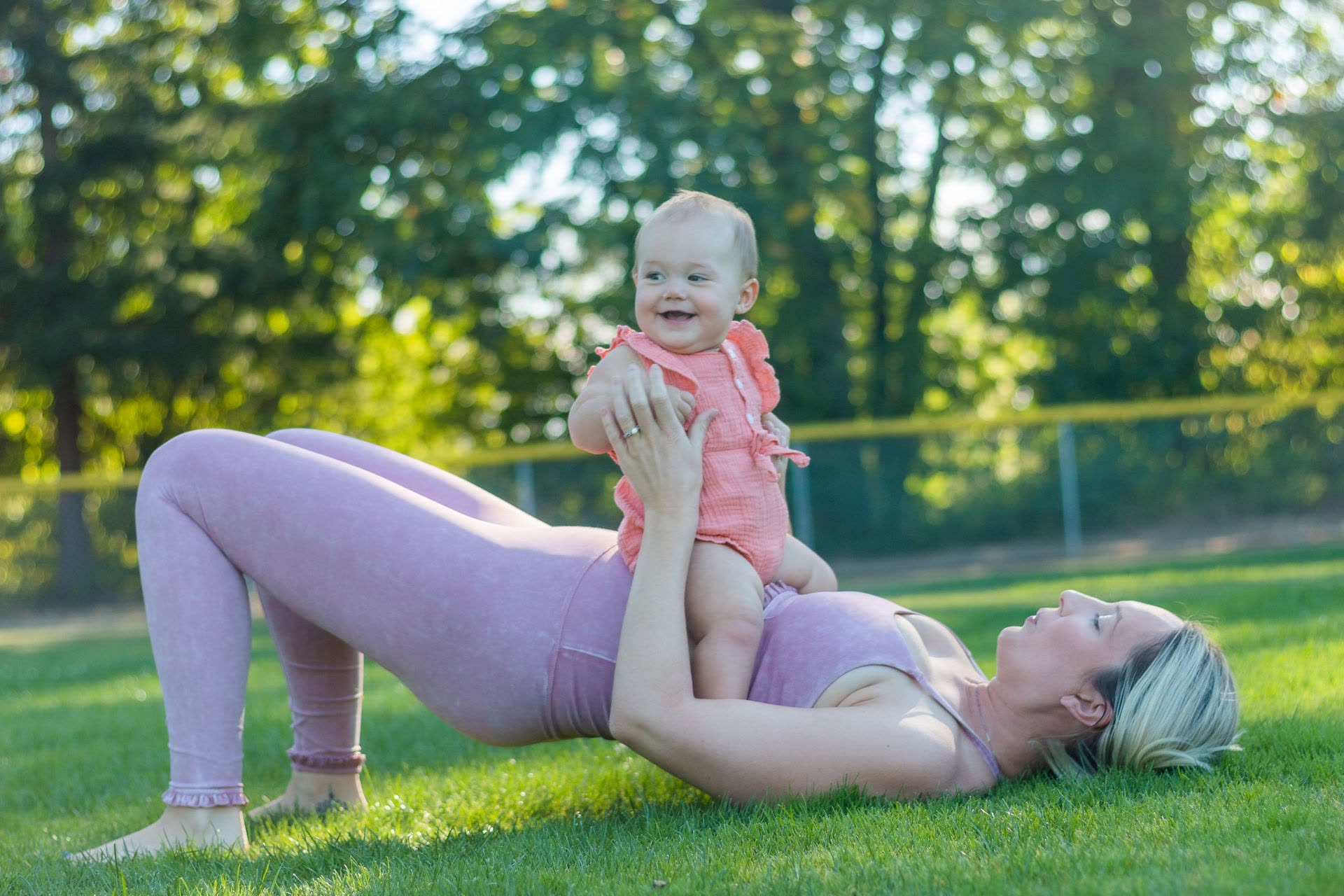 Mamma che solleva il suo bimbo sorridente durante una pratica di Yoga post parto all'aperto